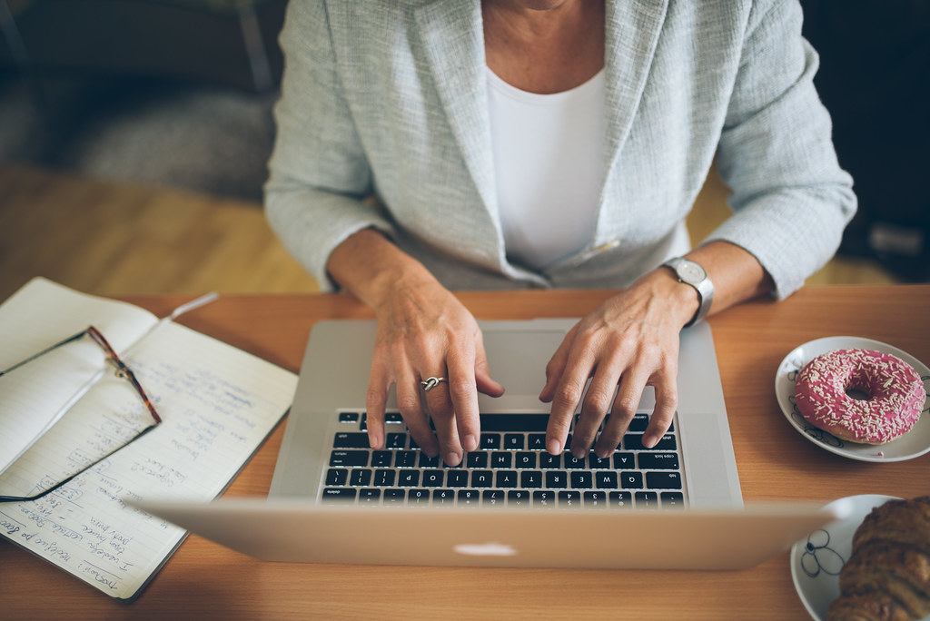 Woman in a blazer typing on a laptop at a desk. 