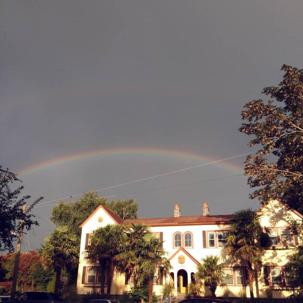 A rainbow in a dark, stormy sky above a white apartment building. 